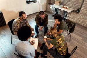 a group of military service members sit in a circle with a therapist and share their issues during their 12-step program 