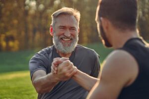 two men outside grab each other hands and smile while participating in group activities in their men's rehab program