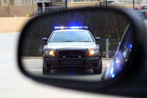 a police care with its lights on in a rearview mirror possibly determining the differences between dui vs. dwi